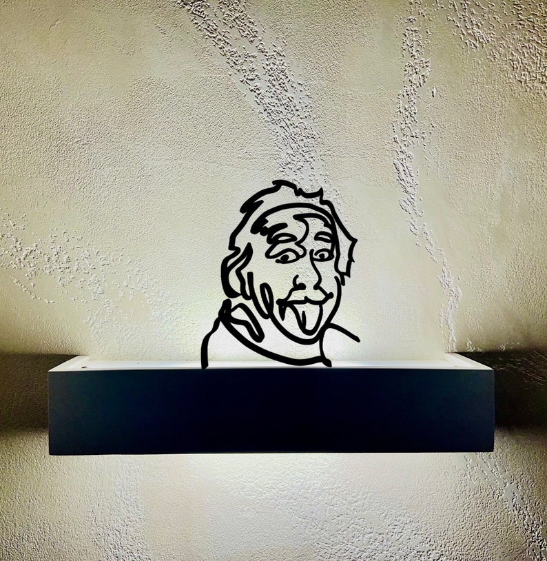 Puede incluir: Un dibujo en blanco y negro de una persona con la lengua fuera, montado en una estanter&iacute;a negra con una luz blanca detr&aacute;s.