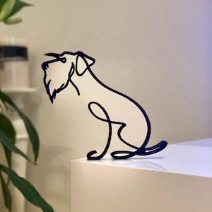 May include: A black metal sculpture of a dog sitting on a white surface. The sculpture is made of a single continuous line.