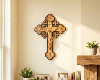 May include: A wooden crucifix with a carved figure of Jesus Christ hangs on a cream-colored wall. The cross has a dark border and decorative elements. The room features a chair, plants, and framed photos, creating a warm, inviting atmosphere.