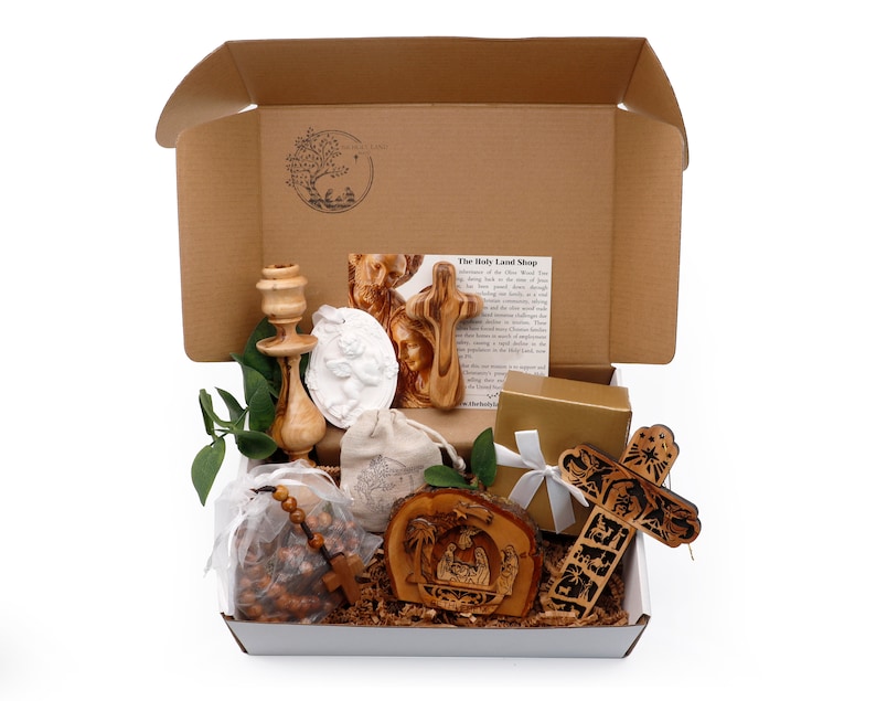May include: A gift box filled with religious items, including a wooden cross, a rosary, a candle holder, and a nativity scene. The box is open, revealing the contents, with a printed card visible inside. The items are arranged on a white surface.
