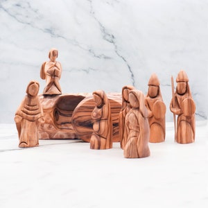 May include: A nativity scene set carved from olive wood. The set includes a manger, an angel, Mary, Joseph, and two shepherds. The figures are all hand-carved and have a rustic, natural look.