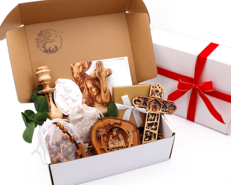 May include: A gift box filled with religious items, including wooden crosses, a nativity scene, and a rosary. The box is open, revealing the contents, with a white box tied with a red ribbon in the background.