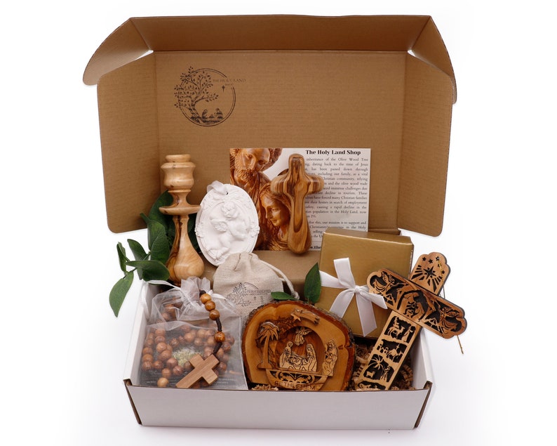 May include: A gift box filled with religious items. Includes a wooden cross, a rosary, a carved wooden nativity scene, a candle holder, a white relief, and other religious artifacts. The box is brown with the text "The Holy Land Shop".