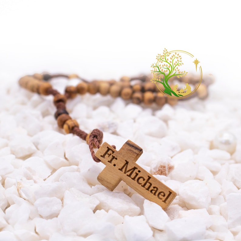 May include: A wooden rosary with a brown cord and wooden beads. The rosary has a wooden cross with the inscription "Fr. Michael" on it.