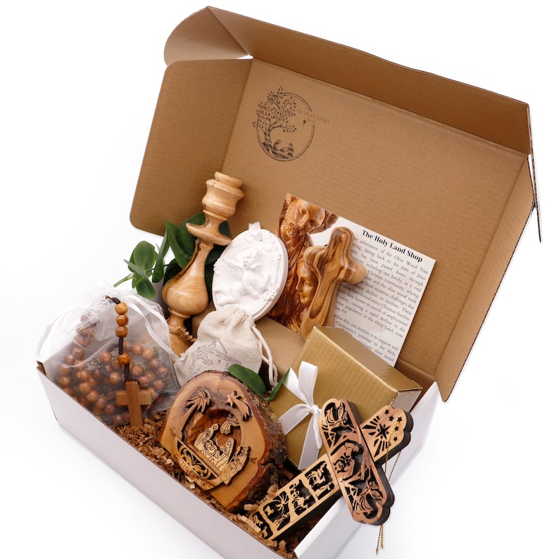 May include: A gift box filled with religious items. Includes a wooden cross, rosary beads, a carved nativity scene, a candle holder, and a white relief sculpture. The box is brown and white, with a logo on the inside.