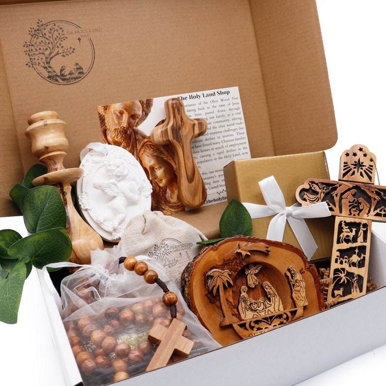 May include: A gift box filled with religious items. Includes a wooden cross, a rosary, a carved wooden nativity scene, and other religious artifacts. The box is brown and white, with a logo on the inside.