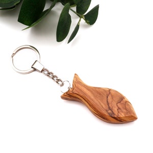May include: A wooden fish keychain with a silver chain and ring. The fish is carved from olive wood and has a natural wood grain.