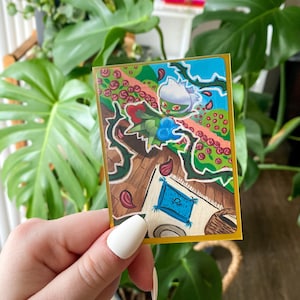 May include: A colorful, illustrated card featuring a green and white character with a floral design. The card has a gold border and depicts a whimsical scene with roses, thorns, and a blue rug. The background includes a lush green plant.