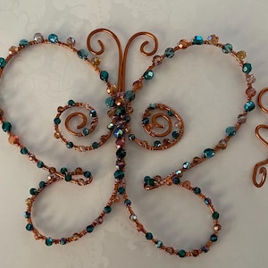 May include: A copper wire butterfly sculpture with teal and iridescent glass beads. The butterfly has a wire body and wings with a swirl design.