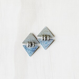 May include: A pair of silver earrings with a geometric triangle design. The earrings are made of textured metal and have a hammered finish.