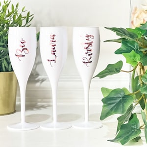 May include: Three white champagne flutes with rose gold lettering. The flutes are personalised with the names "Kristy", "Lauren", and "Bec".