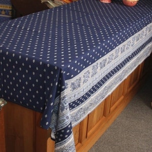 May include: A navy blue tablecloth with a white dotted pattern and a decorative border. The border features floral and paisley designs in white and light blue. The tablecloth is draped over a wooden table, creating a classic and elegant look.