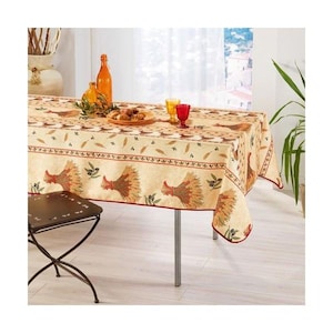 May include: A beige tablecloth with a red border features a repeating pattern of wheat sheaves, olive branches, and roosters. The tablecloth is laid on a table with a metal base and a brown wooden chair.