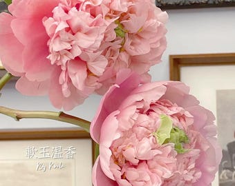 May include: Close-up of two large, pink peony flowers with layered petals. The flowers have a soft, delicate appearance. The image includes text that reads "HOLIDAY" and "2024 Sipring".