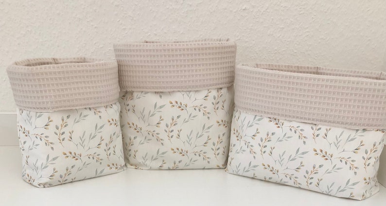 May include: Three beige fabric storage baskets with a white and brown floral pattern. The baskets have a beige waffle-textured top.