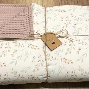 Könnte beinhalten: Eine weiße Decke mit einem floralen Muster aus grauen und gelben Blättern. Die Decke ist gefaltet und mit Schnur und einem braunen Etikett mit der Aufschrift "made with love" gebunden.