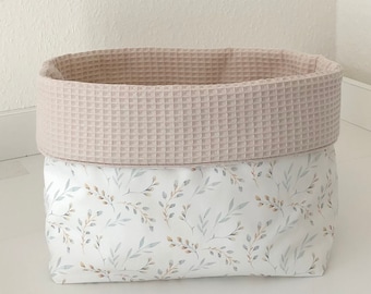 Könnte beinhalten: Ein weißer ovaler Aufbewahrungskorb mit einem beigefarbenen, gewellten Oberteil. Der Korb hat ein Blumenmuster mit kleinen braunen und grauen Blättern.