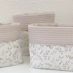 May include: Three fabric storage baskets with a white background and a light gray floral pattern. The top of each basket is a light gray waffle weave fabric.