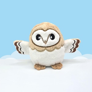 May include: A plush owl toy featuring a tan and white color scheme. The owl has large black embroidered eyes, a small beak, and outstretched wings with brown and white striped patterns. It stands on two small tan feet.