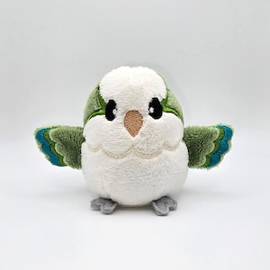 May include: A small, plush green and white bird with embroidered eyes and beak. The bird has a fluffy white body and green wings with blue accents.