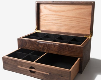 May include: A wooden jewelry box with a hinged lid and a pull-out drawer. The box is made of dark wood with a light wood interior. The box has multiple compartments for storing jewelry.