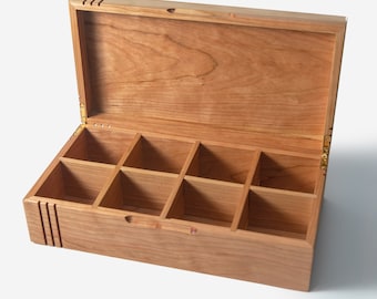 May include: A wooden box with a hinged lid and eight compartments. The box is made of light brown wood with a natural finish. The lid is open and the compartments are empty.