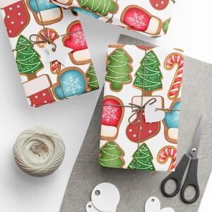 Op de afbeelding: Ingepakte cadeaus met peperkoekontwerpen, waaronder kerstbomen, wanten en sokken, vastgebonden met touw en hartvormige labels. Een bol touw, een schaar en blanco labels zijn ook aanwezig, wat wijst op een vakantiethema.