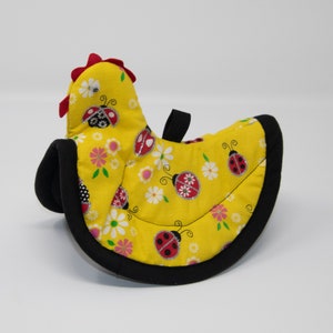 May include: Yellow chicken-shaped pot holder with a black border. The pot holder is decorated with ladybugs and flowers.