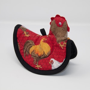 May include: Red, black, and white chicken-themed hot pad with a rooster and hen design. The hot pad is shaped like a chicken and has a black trim.