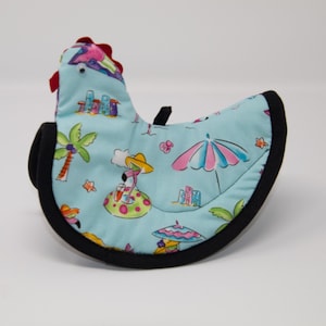 May include: A blue and black chicken-shaped hot pad with a tropical beach print featuring palm trees, flamingos, and umbrellas.