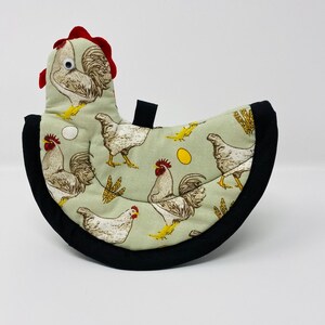 May include: A green and white chicken-themed hot pad with a black border. The hot pad is shaped like a chicken and has a red comb.