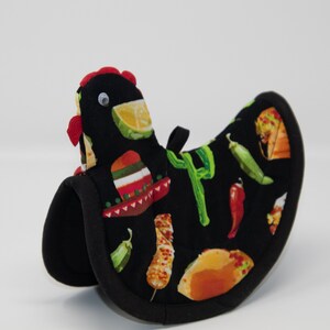 May include: A black oven mitt shaped like a chicken, with a red comb and googly eyes. The mitt is decorated with images of tacos, peppers, limes, and a sombrero. The word "P" is written in green on the mitt.