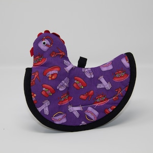 May include: Purple fabric hot pad shaped like a chicken with a red comb and black trim. The chicken is decorated with a pattern of red hats, shoes, and gloves.