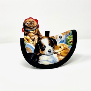 Puede incluir: Un agarrador de olla negro y blanco con un diseño colorido de perros. El agarrador de olla tiene forma de semicírculo y tiene un perro rojo y blanco con un lazo en la cabeza.