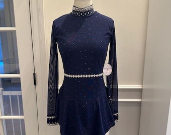 May include: A navy blue figure skating dress on a mannequin. The dress features a high, embellished neckline, long mesh sleeves, and a skirt with a flared hem. The bodice and skirt are adorned with small, scattered embellishments, and a rhinestone belt.