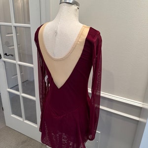 May include: Burgundy long-sleeved skating dress with a sheer nude mesh panel in the back.