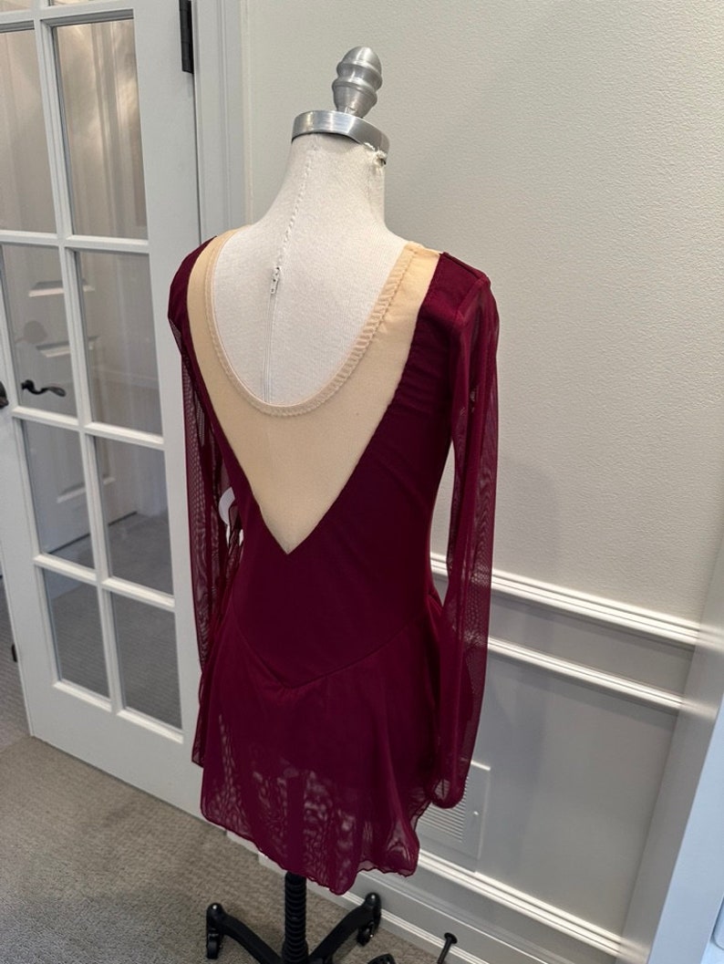 May include: Burgundy long-sleeved skating dress with a sheer nude mesh panel in the back.