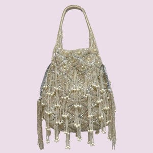 May include: A handbag featuring a scalloped pattern of silver sequins and clear beads. The exterior is adorned with long, dangling fringe strands tipped with small, round, cream-colored faux pearls. It includes a single top handle for carrying.