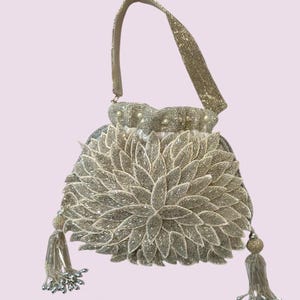 May include: A silver beaded handbag with a floral design. The bag features a beaded handle, a drawstring closure, and two beaded tassels. The floral design is made of layered, leaf-shaped beads. The bag is likely for special occasions.