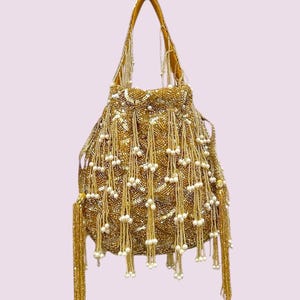 May include: A gold drawstring handbag featuring an intricate pattern of metallic sequins and beads. The exterior is adorned with numerous dangling beaded fringe strands, each tipped with a small white pearl-like bead, creating a textured appearance.
