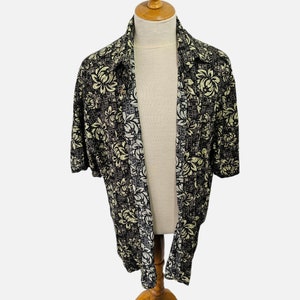 Puede incluir: Una camisa de manga corta con botones y estampado floral en blanco y negro. La camisa tiene un corte holgado y un cuello.