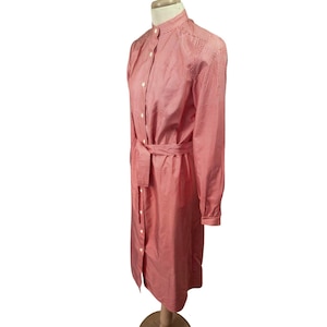 May include: A red and white gingham print dress with long sleeves and a matching belt. The dress has a button-down front and a mandarin collar. The dress is displayed on a mannequin.