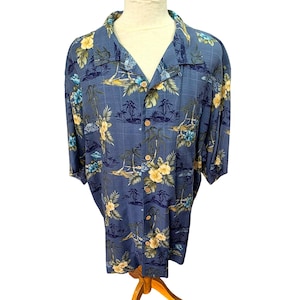 Può includere: Camicia blu con bottoni con un motivo floreale tropicale e palme. La camicia presenta maniche corte, scollo a V e bottoni in legno. Il design include fiori gialli e blu, palme e una scena di spiaggia.