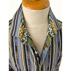 May include: A long-sleeved button-down shirt featuring a vertical striped pattern in black, blue, white, and yellow. The inner collar and inner placket display a vibrant, multi-coloured stained glass window print with geometric shapes.