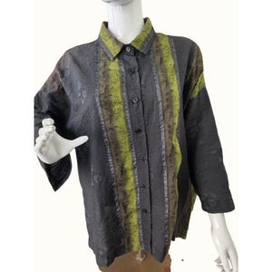 Pode incluir: Uma camisa de botões com uma base cinza-carvão escuro e um acabamento de tecido texturizado e amassado. Um painel vertical de tecido verde-limão com um padrão floral escuro percorre a frente, complementado por uma gola verde-limão a combinar.