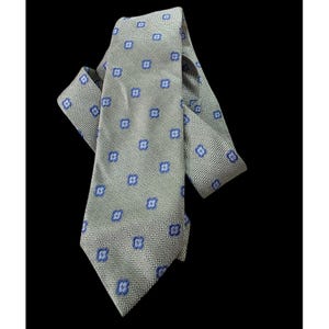 以下が含まれることがあります： 青い花の模様が繰り返される、明るい緑色のネクタイ。 ネクタイはテクスチャード加工された生地で作られており、黒い背景に表示されています。 ネクタイは結ばれており、角度が付けられており、そのデザインが際立っています。