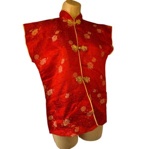 May include: A sleeveless red Chinese-style top with gold trim and floral embroidery. The top features frog closures and a mandarin collar. The fabric has a subtle sheen, and the overall design is traditional and elegant.