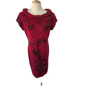 May include: A red, short-sleeved dress with a cowl neck. The dress features a black floral pattern across the front and shoulders. The dress is displayed on a mannequin.