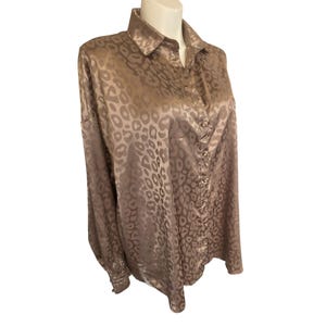 Pode incluir: Camisa bege com estampa de leopardo e botões. A camisa de manga comprida tem gola e botões na frente e nos punhos. A camisa é exibida em um manequim.