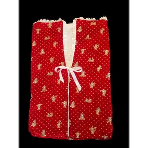 May include: A red baby blanket with a pattern of small white dots and teddy bears. The blanket has a white ribbon tie closure and is trimmed with white lace. The blanket is made of a soft, plush material.